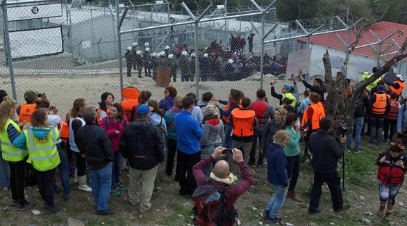 مهاجرون ورجال شرطة أمام باب مخيم موريا في اليونان(رويتر)