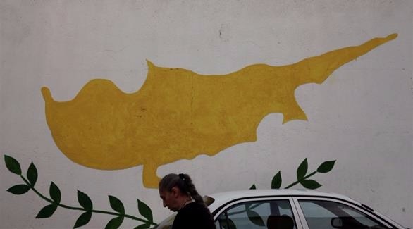 امراة تمر بالقرب من رسم للعلم القبرصي على أحد الجدران في نيقوسيا (رويترز)