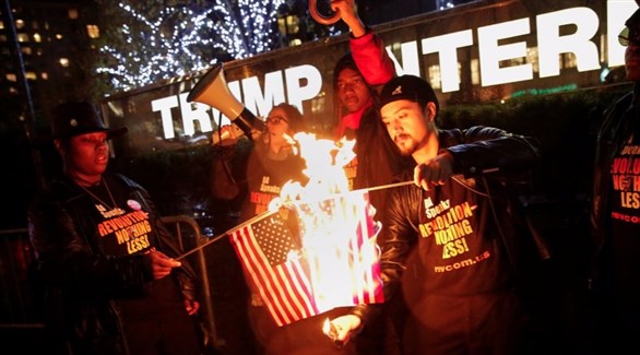متظاهرون يحرقون العلم الأمريكي أمام مبنى ترامب (رويترز)
