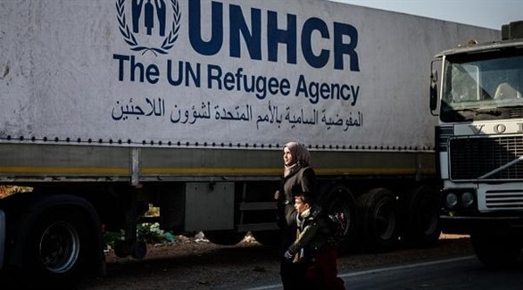سيدة سورية تمر بصحبة طفلها من أمام شاحنة مساعدات أممية (أرشيف)