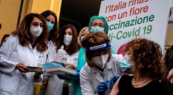 ممرضات حول إيطالية قبل تطعيمها تحت لافة عليها شعار إيطاليا تُولد من جديد (أرشيف)