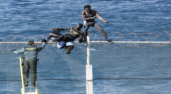مهاجران يحاولان تجاوز السياج حول جيب سبتة تحت أنظار عنصر من الحرس المدني الإسباني (أرشيف)